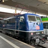 111 054-3 wurde 1976 bei Henschel gebaut und bis 2022 bei der DB im Einsatz (zuletzt bei DB Regio). Die Lok wurde später an TRI verkauft und  ist seit Dezember 2023 in einer Lackierung unterwegs, die an die ursprüngliche Lieferzustand der Baureihe 110 erinnert. Die Loks der Baureihe wurden damals ozeanblau/beige ausgeliefert. Die Lok wird mit Personenwagen an Unternehmen für den  Ersatzverkehr vermietet - wie hier im Düsseldorfer Hbf (23.8.2025) - DB - Klassiker